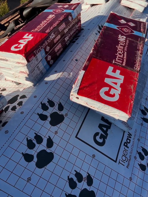 Bundles of GAF Timberline NS Charcoal shingles staged on GAF Tiger Paw underlayment