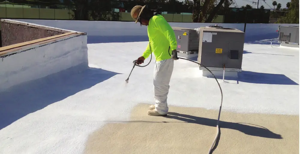 Worker spraying white roof coating onto a commercial flat roof