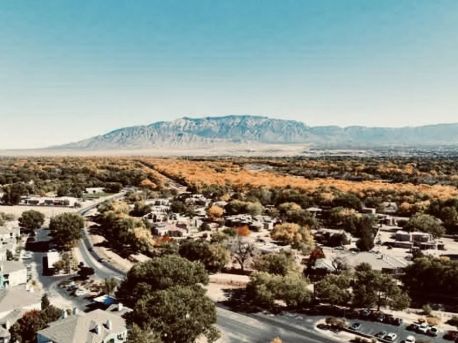 Cottonwood trees and adobe homes near the bosque, with Sandia Mountains in the background
