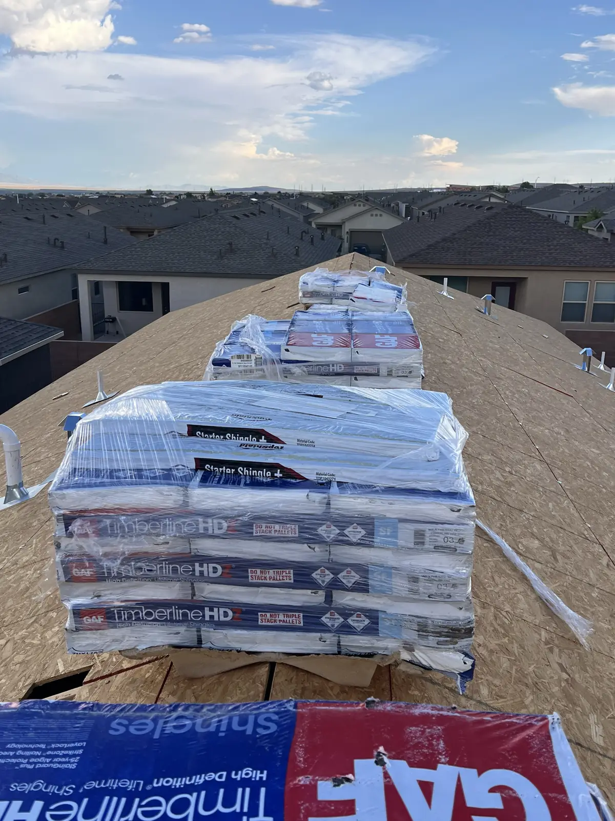 Pallets of GAF Timberline HDZ shingles and starter strips staged along new roof decking during a Timberwolf roof replacement on an Albuquerque-area home